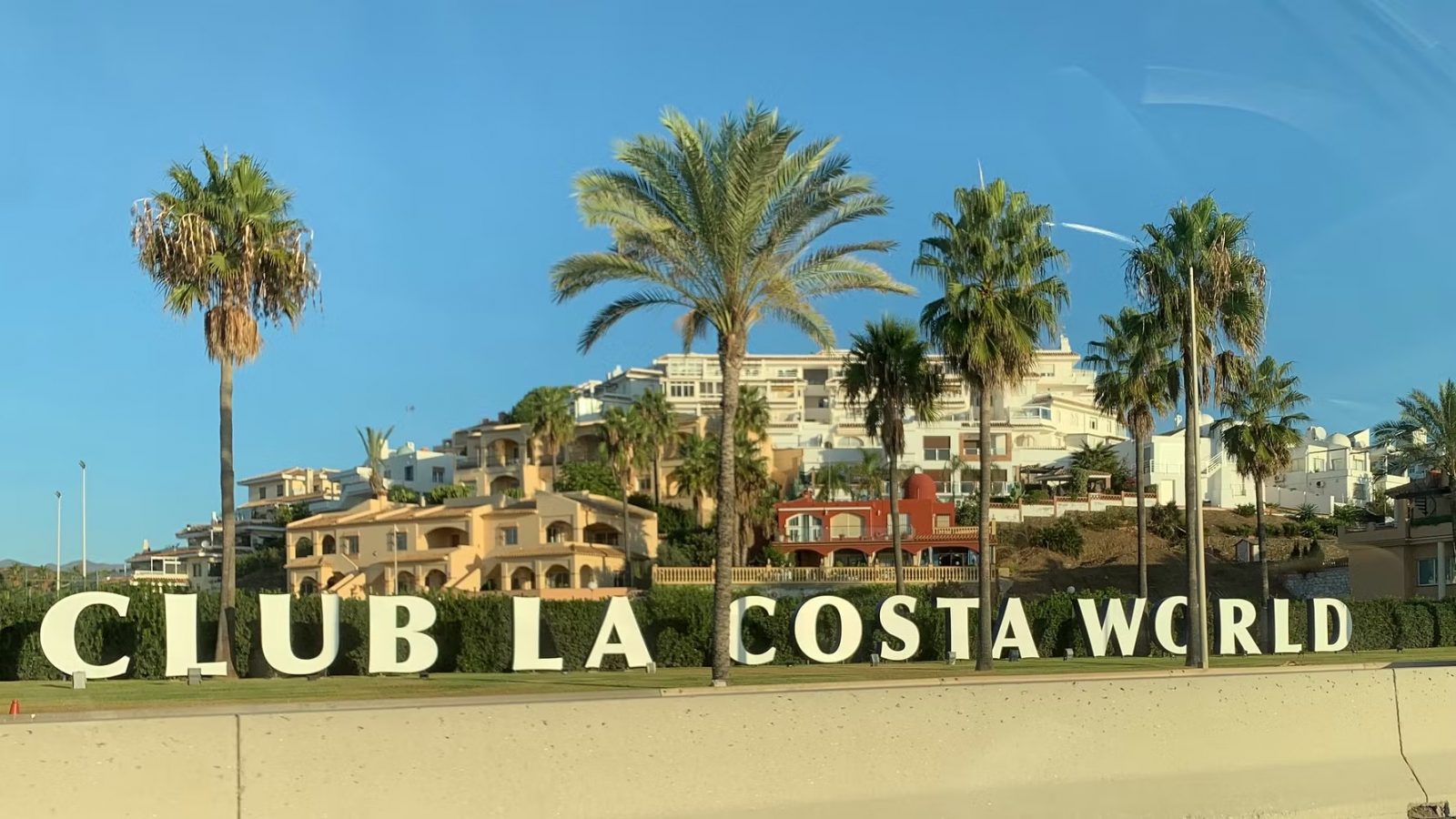Large “CLUB LA COSTA WORLD” sign in front of palm trees and resort buildings under a clear blue sky