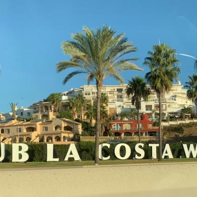 Large “CLUB LA COSTA WORLD” sign in front of palm trees and resort buildings under a clear blue sky